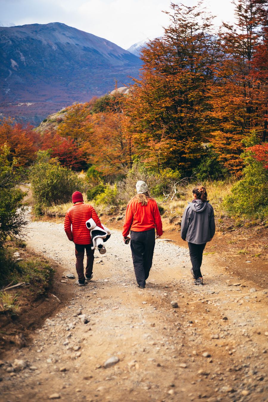 Tres personas caminando por sendero de otoño con cerros al fondo